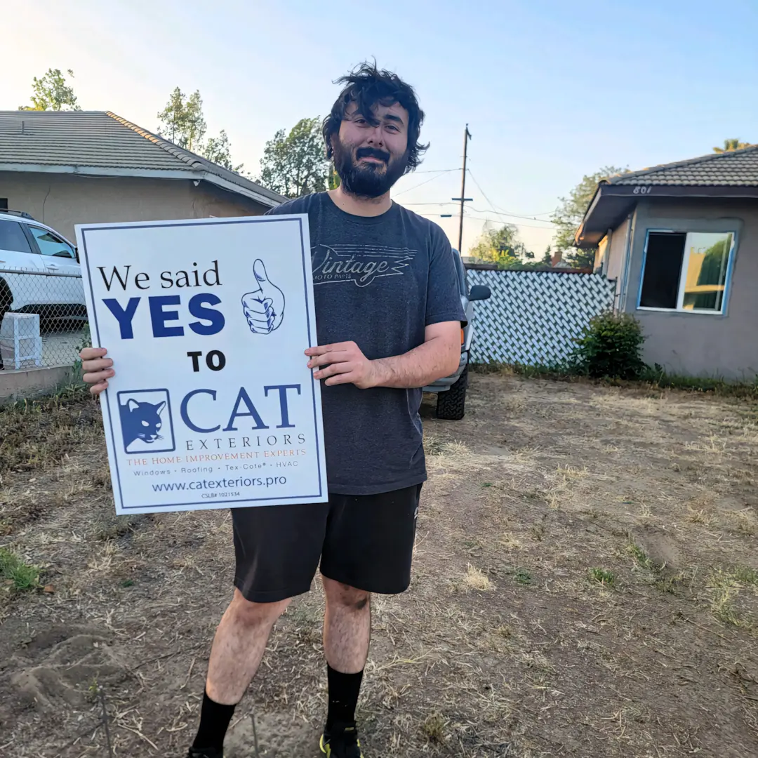 A full color 1080x1080 webp image of a happy CAT Exteriors client in front of their home.