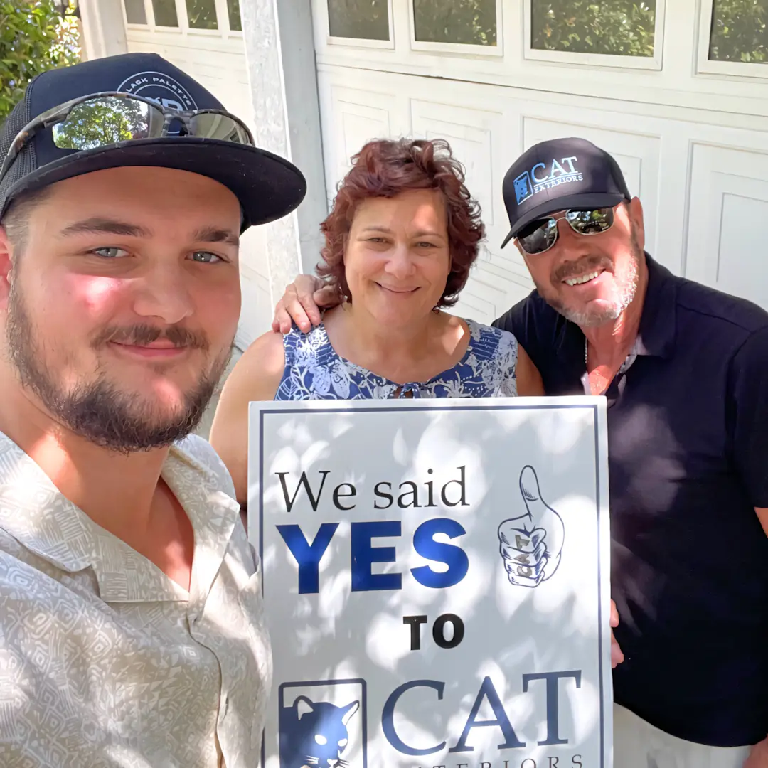 A full color 1080x1080 webp image of a CAT Exteriors representative taking a photo with a happy client at their home.