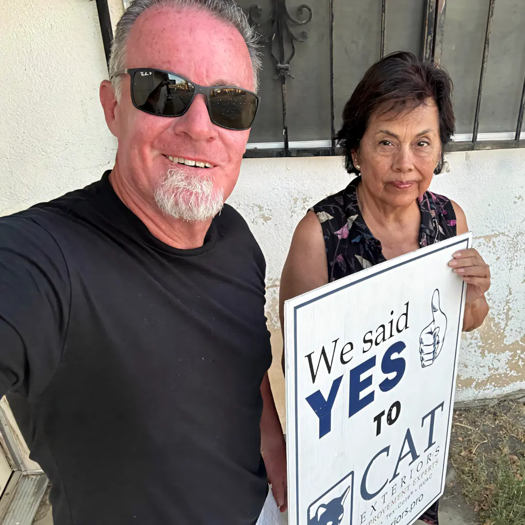 A full color 1080x1080 webp image of a CAT Exteriors representative taking a photo with a happy client at their home.