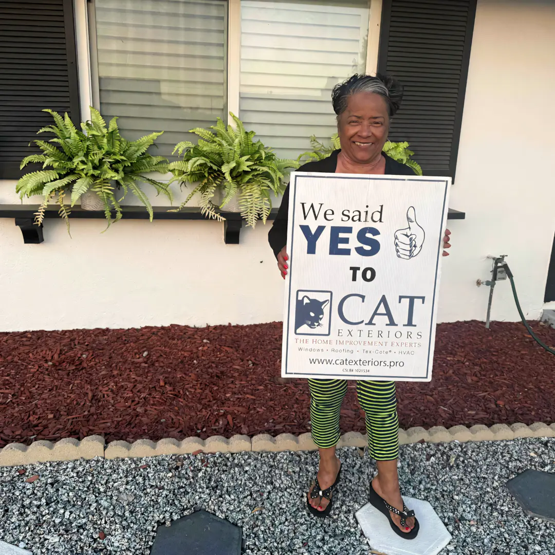 A full color 1080x1080 webp image of a happy CAT Exteriors client in front of their home.