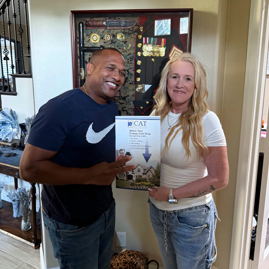 A full color 1080x1080 webp image of a happy CAT Exteriors client in front of their home.